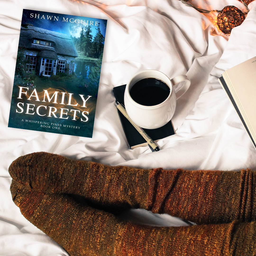 Book titled 'Family Secrets' by Shawn McGuire on a bed with a cup of coffee and socks.