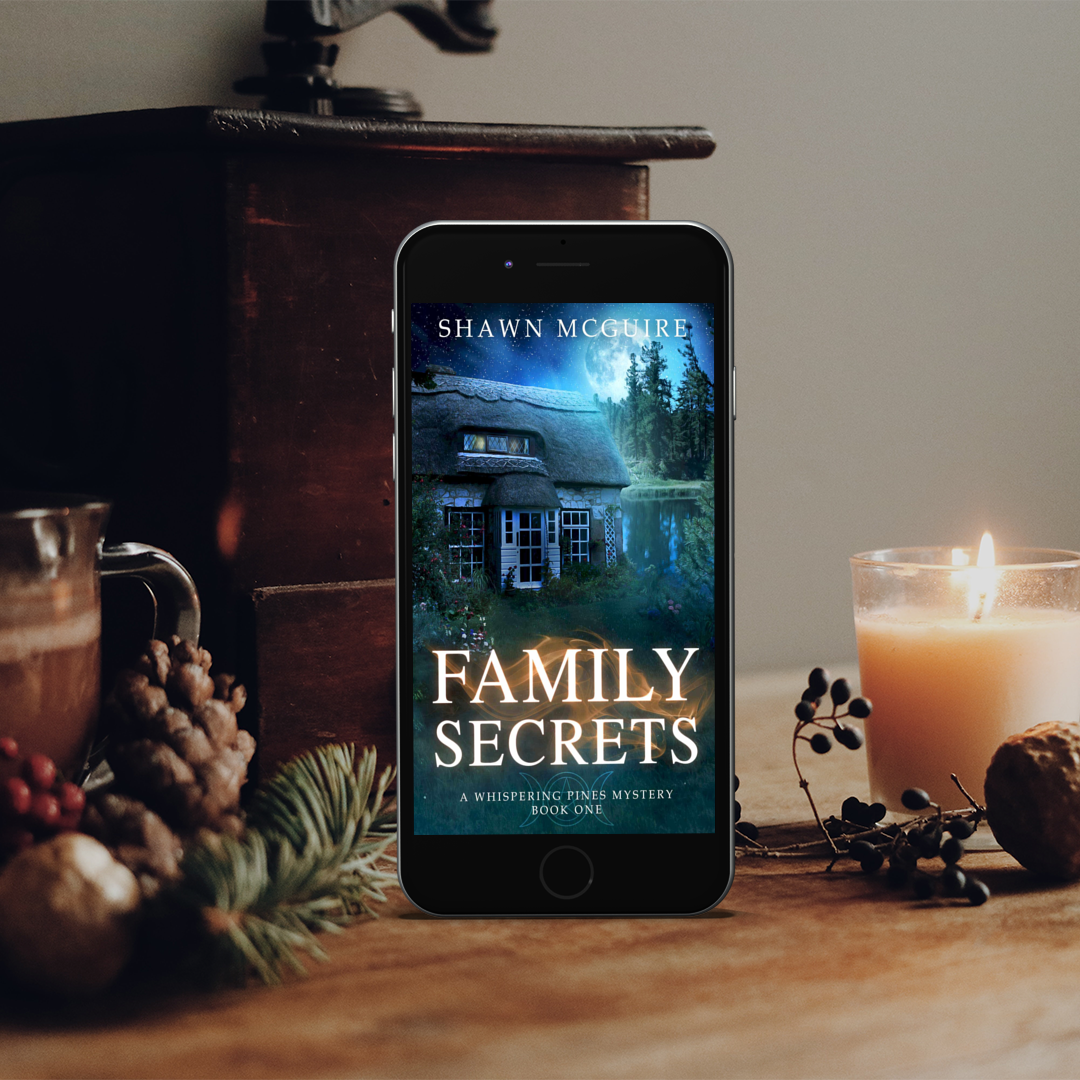 Phone displaying 'Family Secrets' book cover with a cozy setting of a candle, mug, and pine branches.