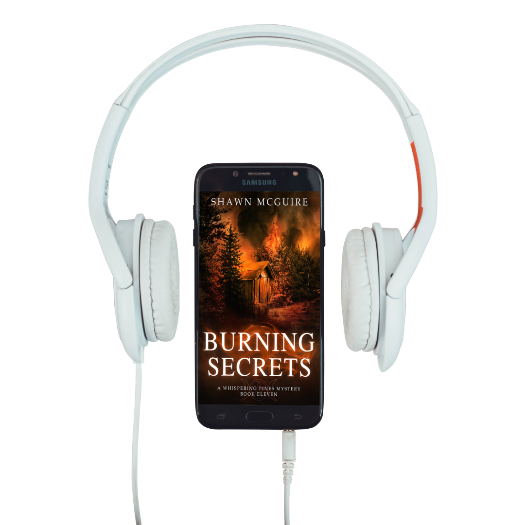 Audiobook cover on cellphone of Shawn McGuire's cozy murder mystery set in Whispering Pines, featuring a burning forest and shack.