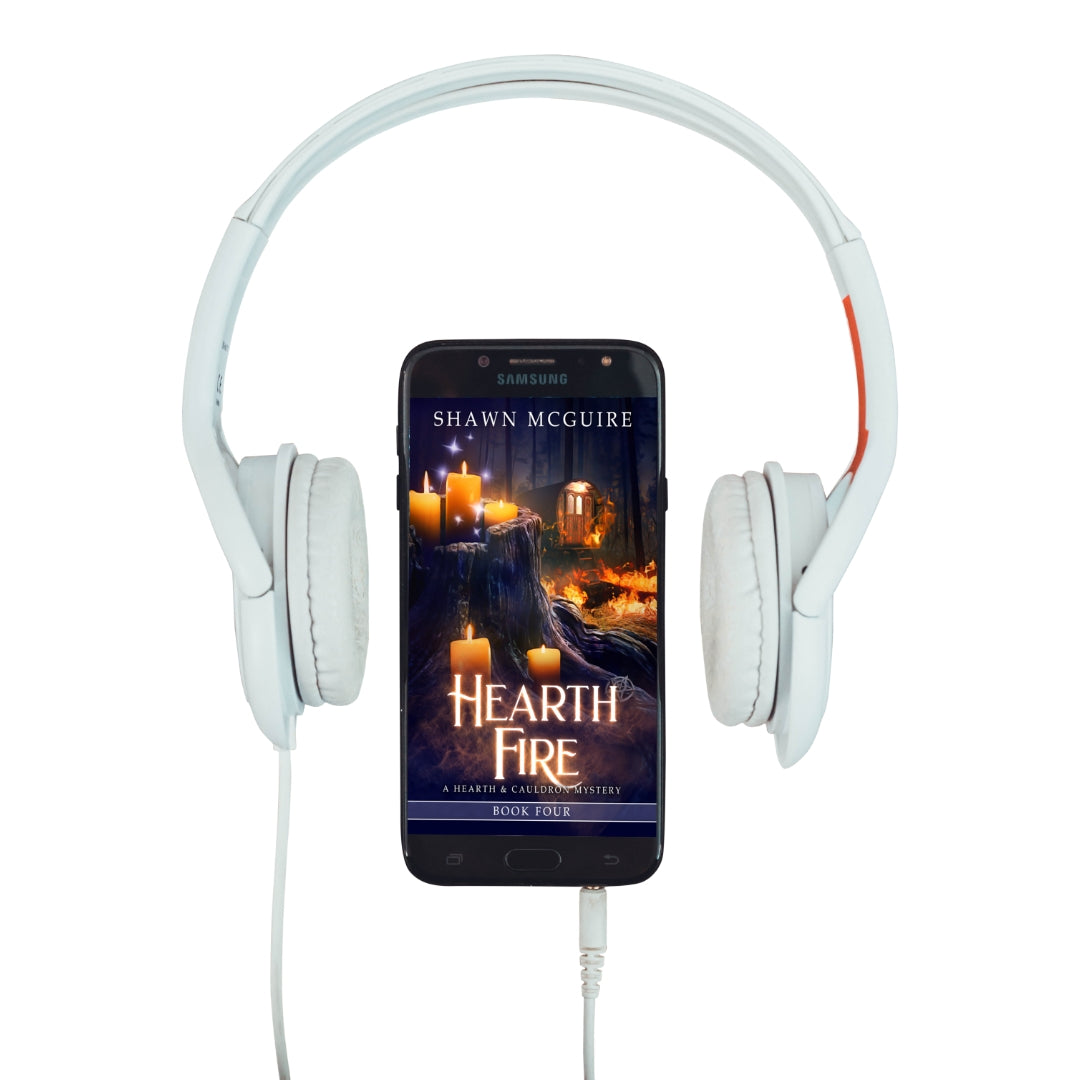 Audiobook cover on cellphone of Shawn McGuire’s witch cozy midlife mysteries with a burning fortune teller wagon in background and lit candles on tree stump in foreground.