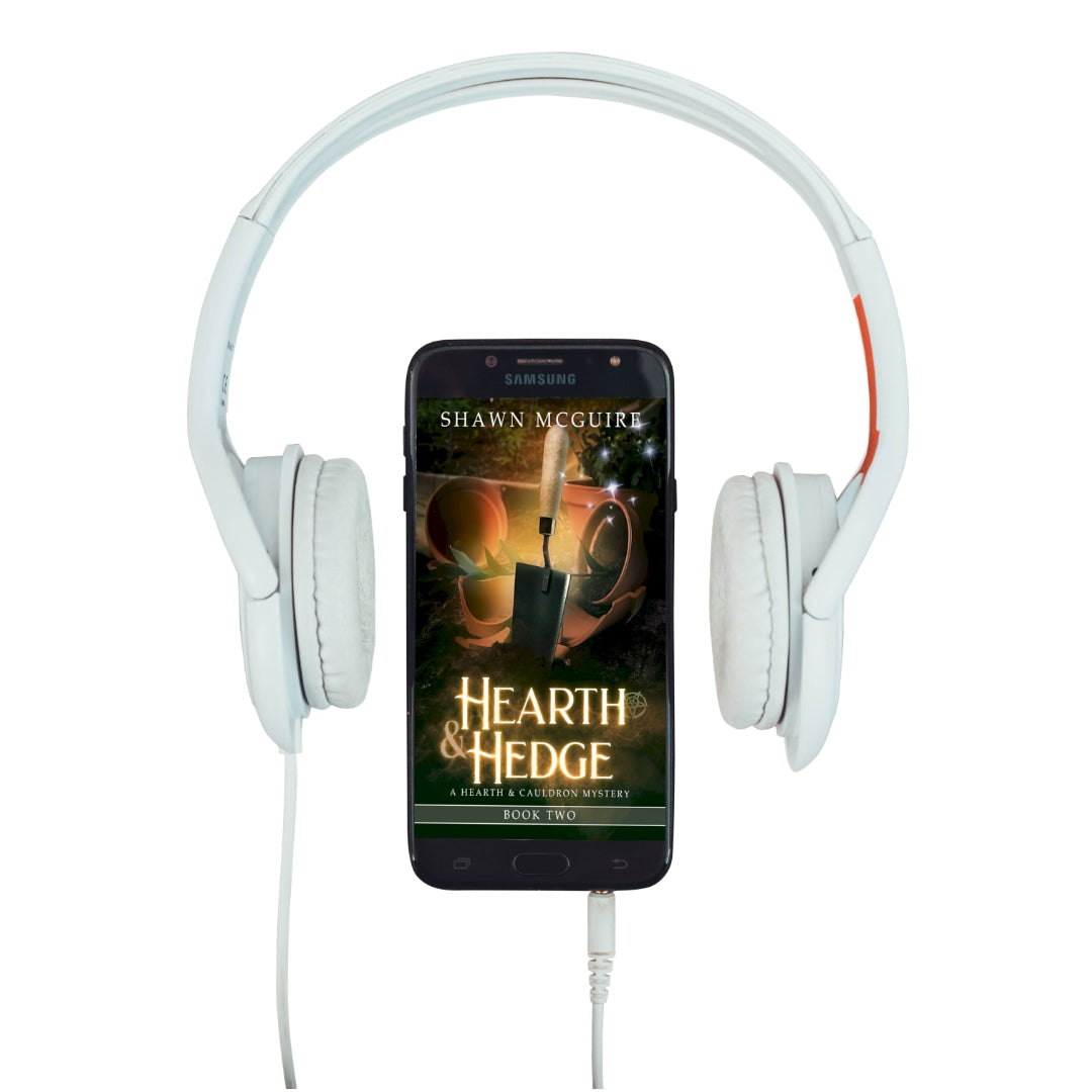Audiobook cover on cellphone of Shawn McGuire’s witch cozy midlife mysteries with broken plant pots and a hand trowel.