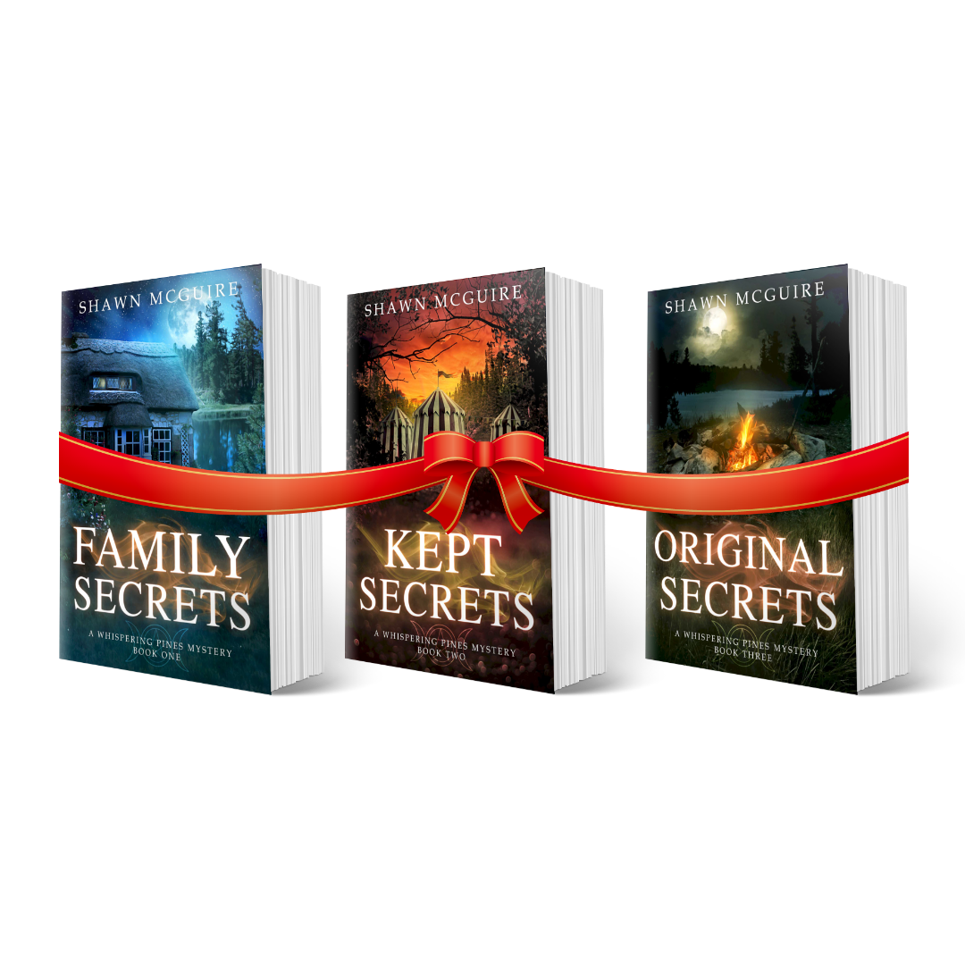 Paperback covers of Shawn McGuire’s 3-book cozy murder mystery series collection books 1-3 with a gift bow.
