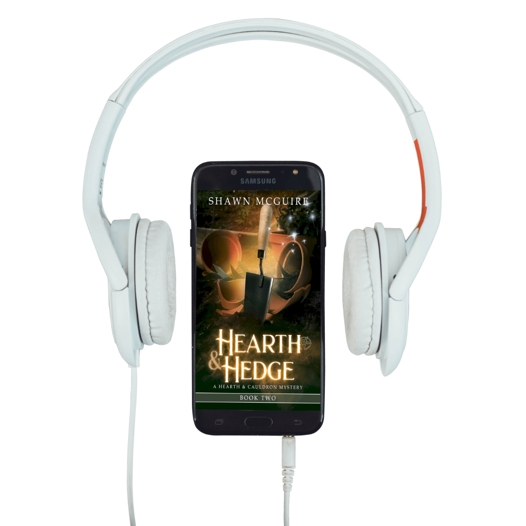 White headphones with a smartphone displaying 'Hearth & Hedge' book cover.
