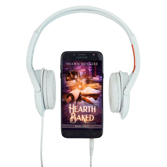 White headphones with a smartphone displaying 'Hearth Baked' by Shawn McGuire