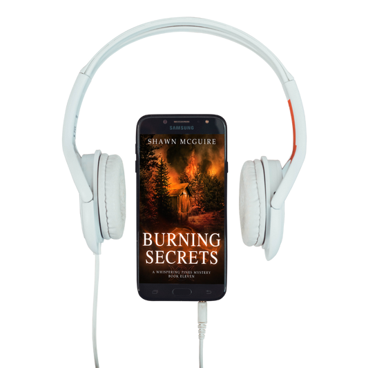 Audiobook cover on cellphone of Shawn McGuire's cozy murder mystery set in Whispering Pines, featuring a burning forest and shack.