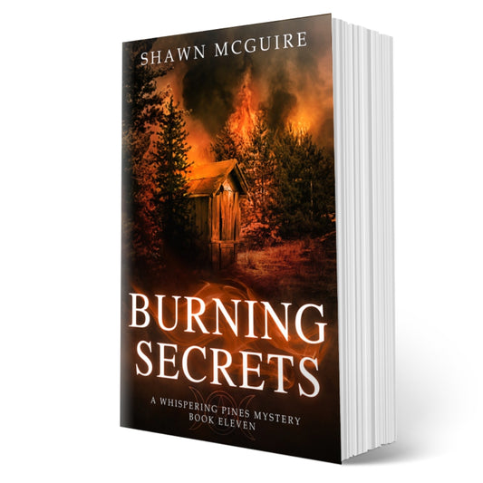 Cover of Shawn McGuire's cozy murder mystery set in Whispering Pines, featuring a burning forest and shack.
