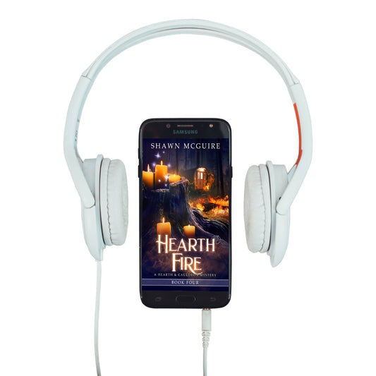 Audiobook cover on cellphone of Shawn McGuire’s witch cozy midlife mysteries with a burning fortune teller wagon in background and lit candles on tree stump in foreground. 