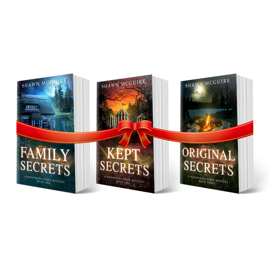 Paperback covers of Shawn McGuire’s 3-book cozy murder mystery series collection books 1-3 with a gift bow.
